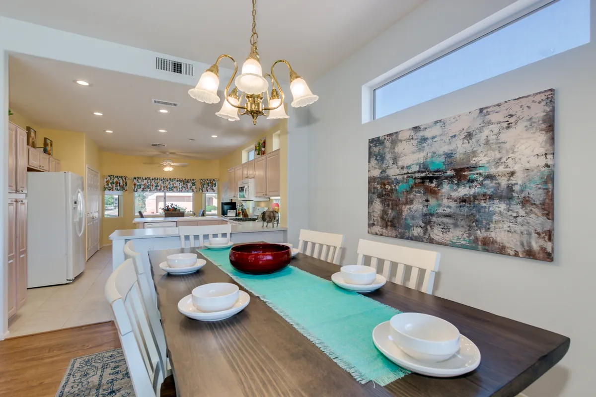 A warm, inviting dining area featuring an elegant dining table beneath a sparkling chandelier, complemented by tasteful artwork on the wall. The ambiance is perfect for family dinners, celebrations, and lively gatherings.