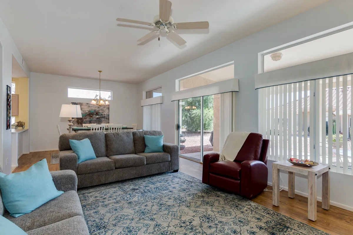 A comfortable living area featuring a sofa with turquoise cushions, a red accent chair, and a view into the adjacent dining area. The room is well-lit and arranged for both relaxation and socializing.