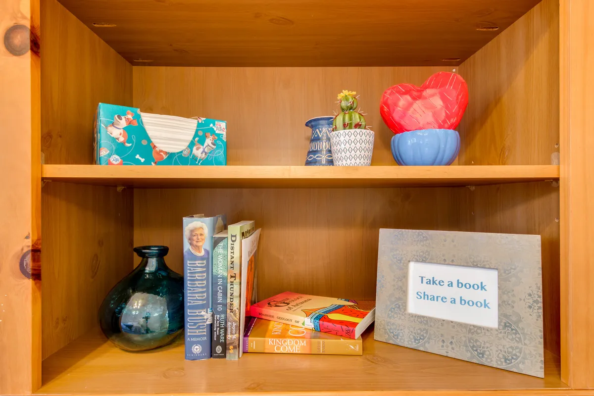 An inviting interior nook filled with colorful books, decorative pots, and a playful message sign. The area suggests a welcoming spot for reading, hobbies, or quiet work, making it perfect for either an office nook or creative pursuits.