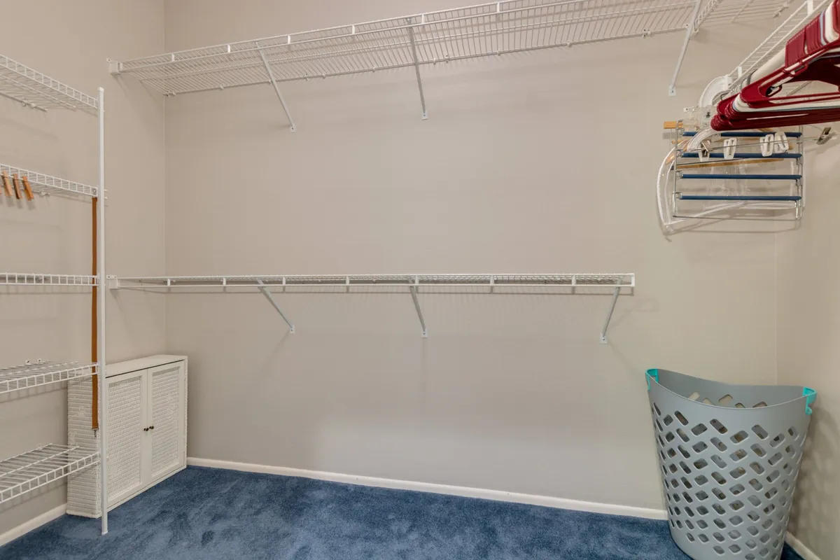 A compact laundry room with blue carpet, wire shelving, and a laundry basket—ideal for organizing clothing and household items. The functional setup offers plenty of storage and a clean, tidy atmosphere, underscoring the home’s attention to practical details.