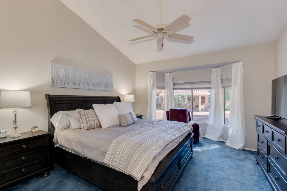 A calm and inviting bedroom with a comfortable bed, window with curtains, nightstand, dresser, and a cozy accent chair. Natural light streams into the space, creating a welcoming environment for guests or family.