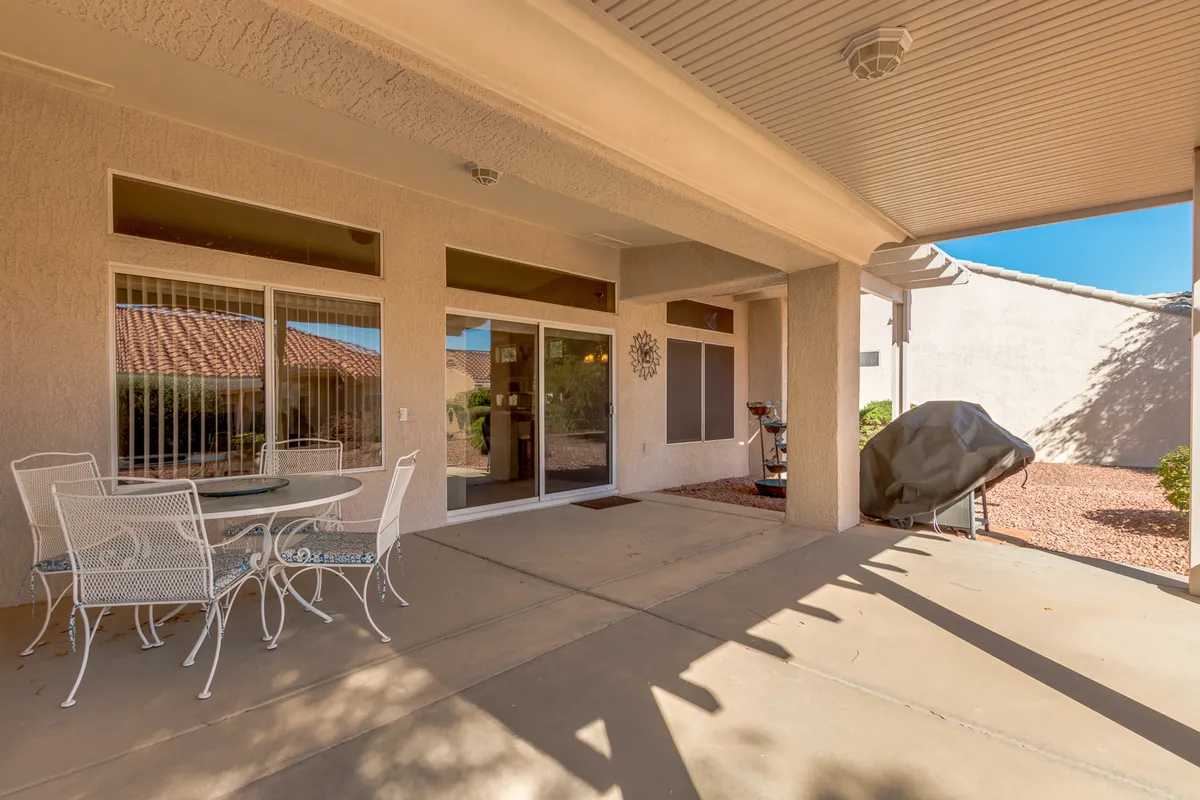 A casual and welcoming backyard setup featuring a table and chairs under a covered area, a nearby grill, and a sliding glass door that hints at easy indoor-outdoor transitions. Decorative touches and greenery create a warm, sociable environment for outdoor meals and get-togethers.