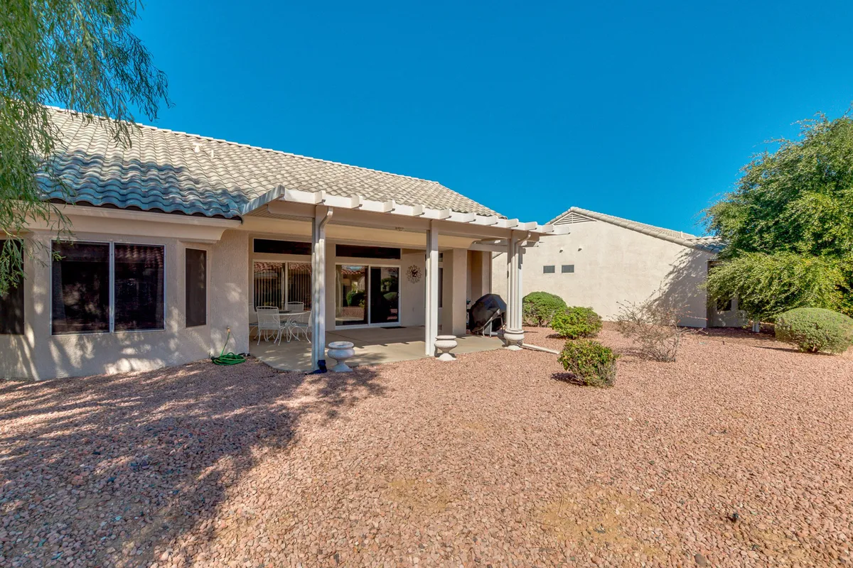 A spacious covered patio area featuring lawn chairs, a grill, and desert landscaping. The setup is ideal for outdoor dining, socializing, and unwinding while taking in sunset views or stargazing on clear Arizona evenings.