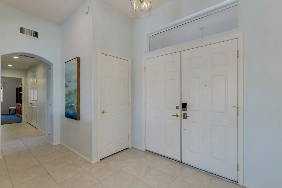 A bright, inviting entryway with double front doors, tasteful artwork on the wall, and a contemporary ceiling light fixture. The scene suggests the welcoming experience of greeting guests as they enter the home.