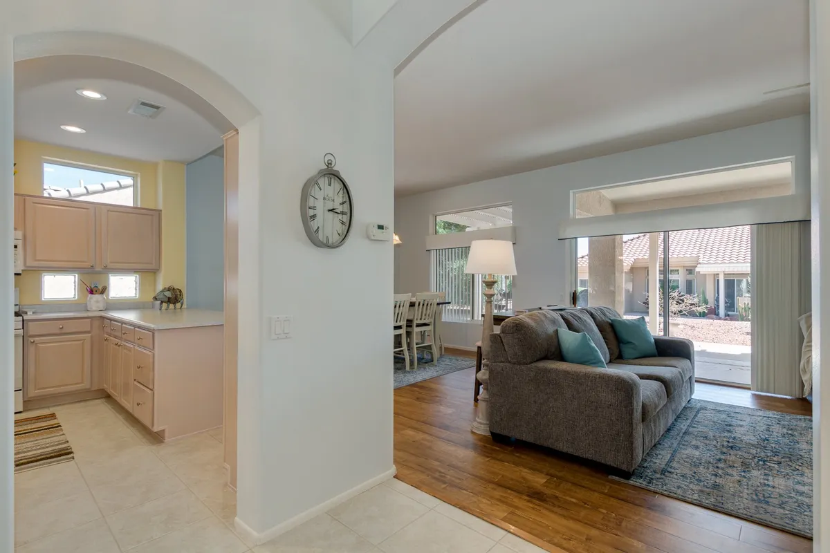 A wide, cozy view encompassing the kitchen area, living room with a comfortable sofa, and a dining table, all arranged within a single open-concept space. Natural light streams in, highlighting the seamless flow between the family room, kitchen, and dining area.