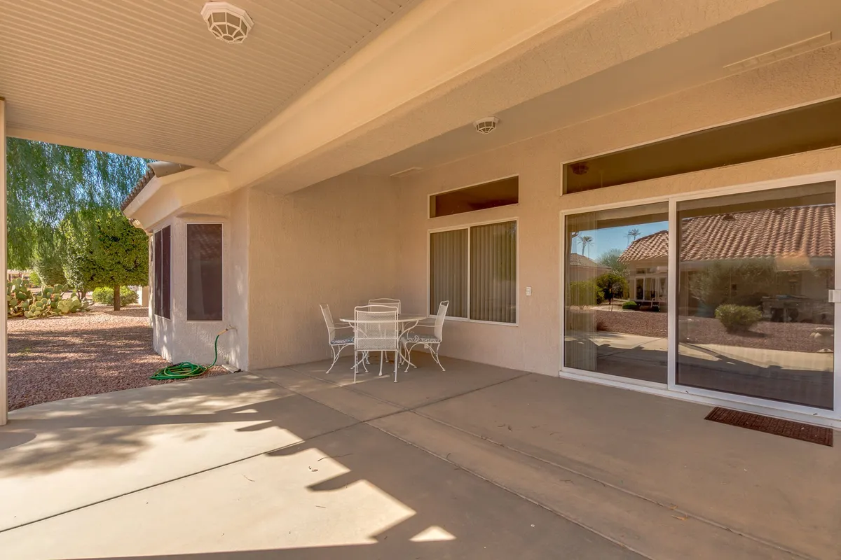 A serene backyard scene with an outdoor table and chairs set amid a landscaped garden and large windows overlooking the space. The tranquil mood suggests opportunities for outdoor dining, relaxing in the shade, or enjoying sunset views.