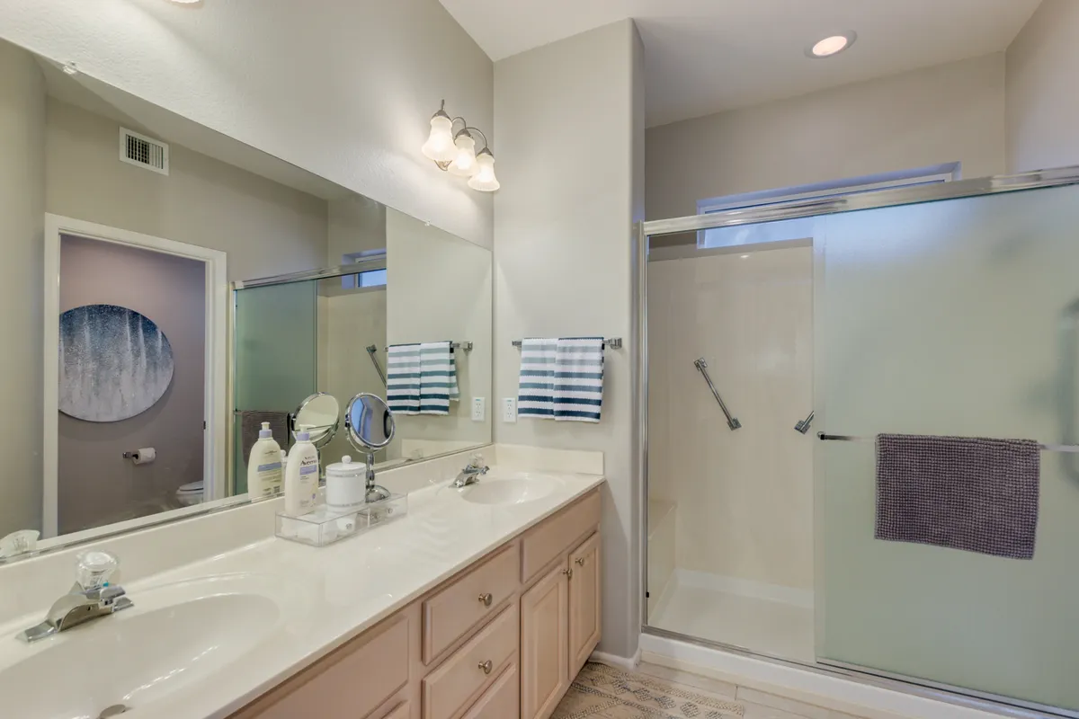 A modern bathroom with a double vanity, large mirror, and a glass-enclosed walk-in shower. The space feels fresh, organized, and designed for both comfort and efficiency during daily routines.