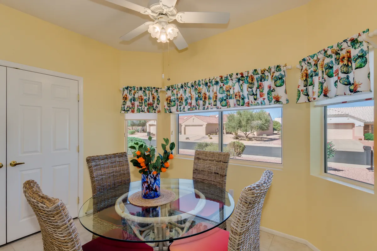 A sunlit breakfast nook with a round glass dining table, vibrant floral window treatments, and a bright centerpiece, creating a joyful space for casual meals, morning coffee, or relaxed conversations with family and friends.