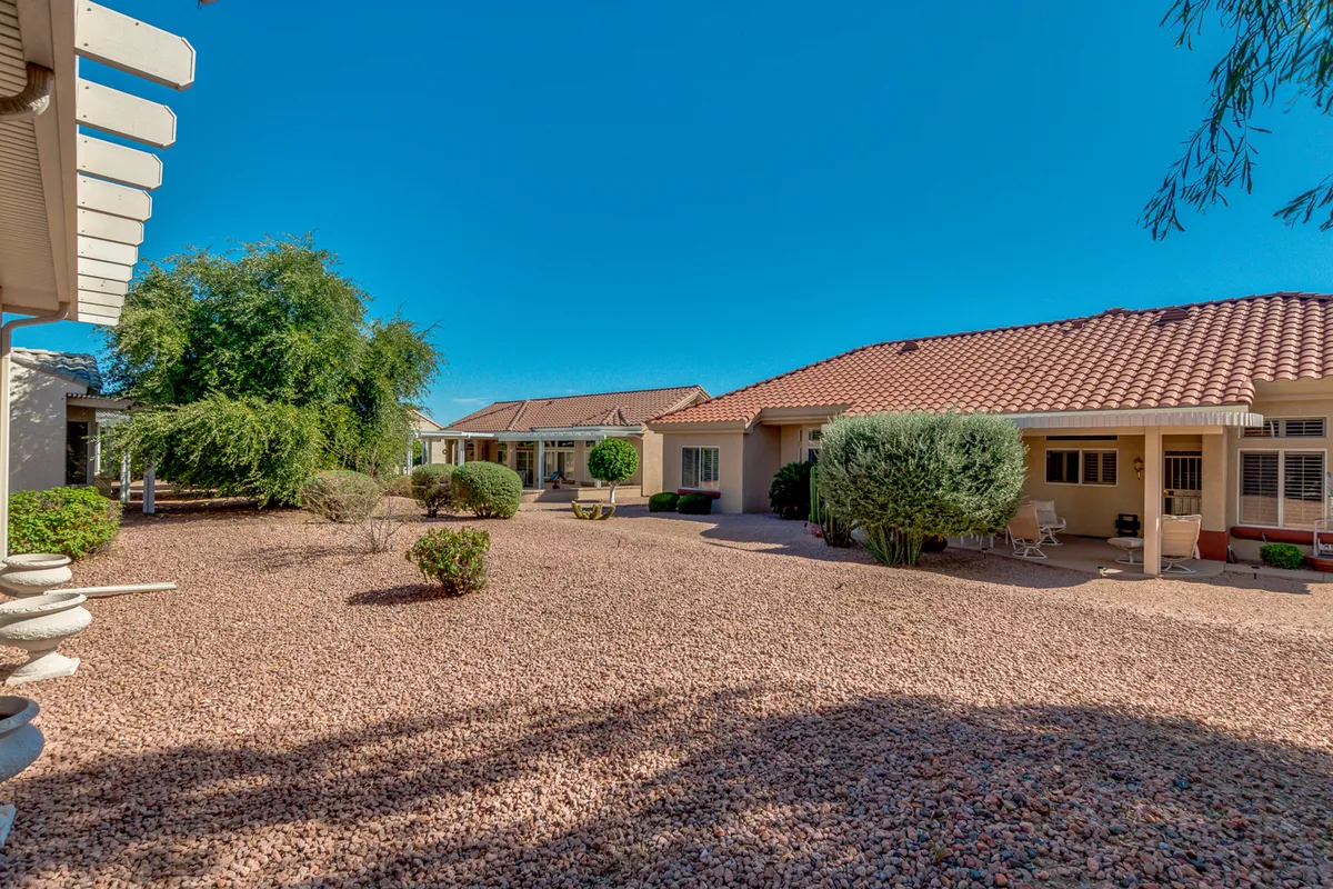 This exterior image features well-maintained landscaping, a spacious courtyard, lush plant life, and neighboring tile-roofed homes. The scene conveys a tranquil, sociable atmosphere with spaces for morning coffee or evening gatherings under the open sky.